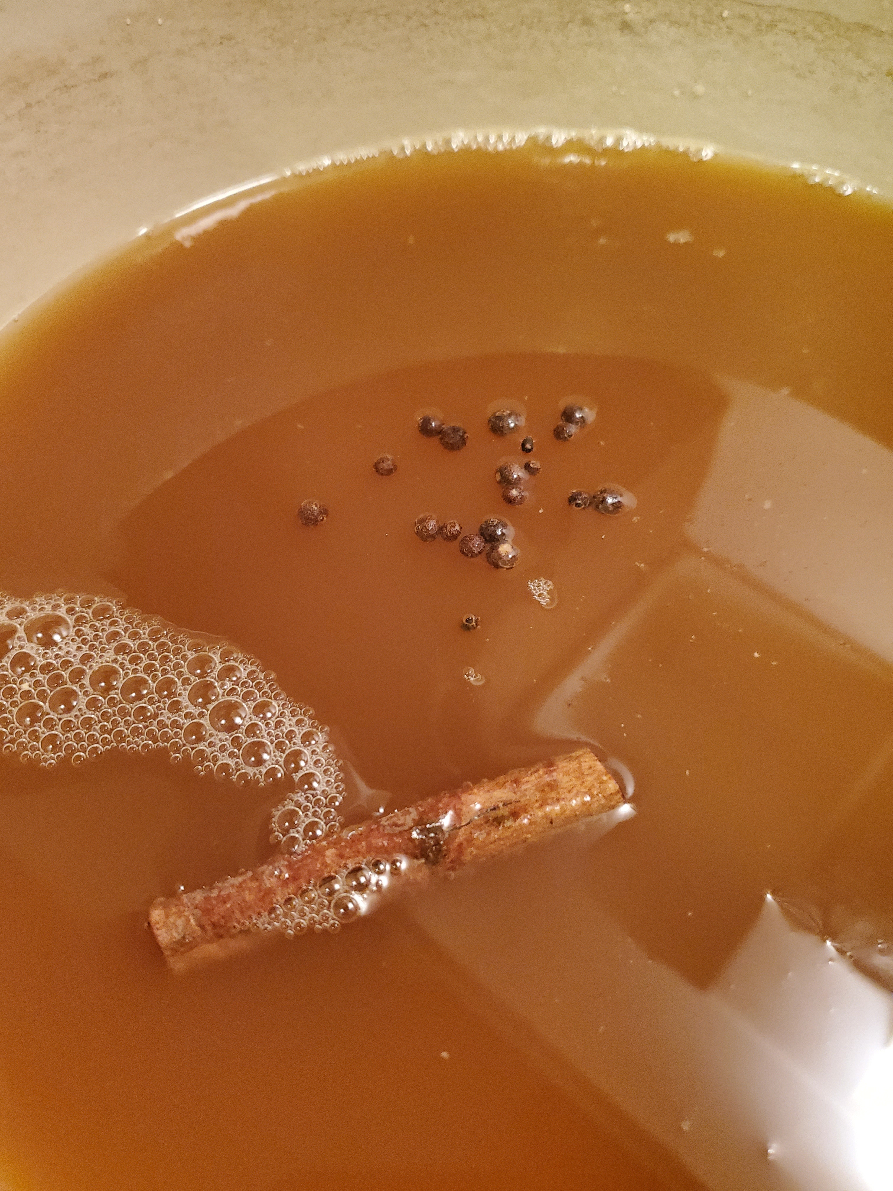 Close-up of cider - cinnamon sticks and whole allspice floating in cider.
