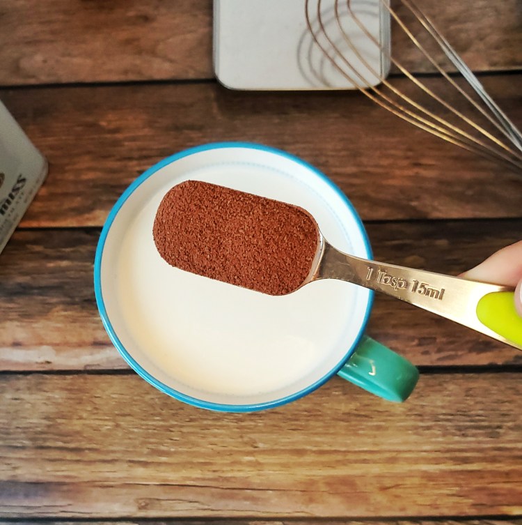 image of a tablespoon of mix held over a hot cup of milk